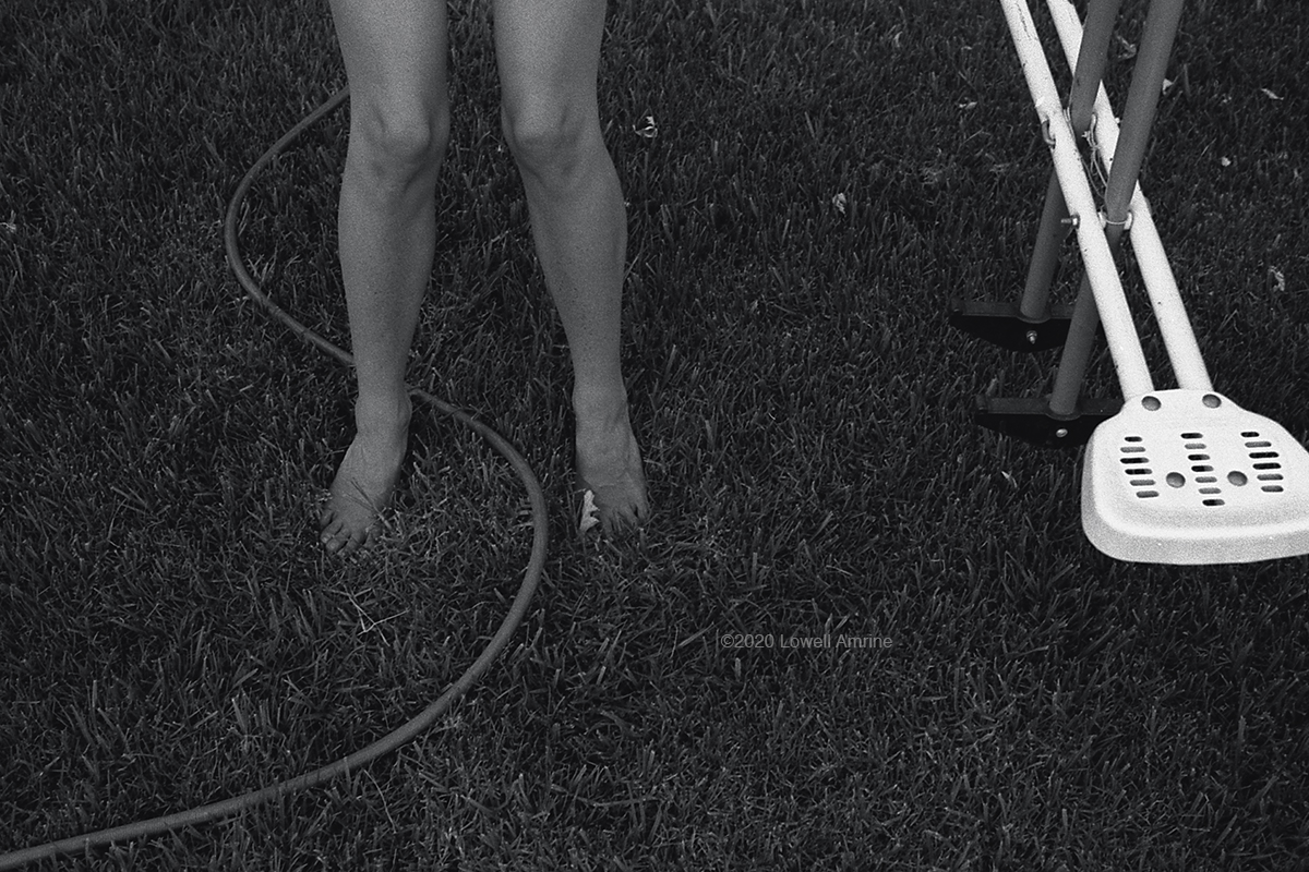 Linda's legs with garden hose between feet on grass and part of swing set